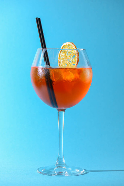 A glass of fruit liqueur in wine glass with a piece of lemon and black plastic straw isolated on pastel blue background. Summer alcohol drink. Copy space. - Фото, изображение