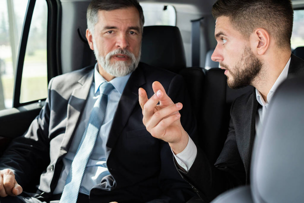 colegas de negocios discutiendo ideas de negocios mientras están sentados en el asiento trasero del coche o taxi
. - Foto, imagen