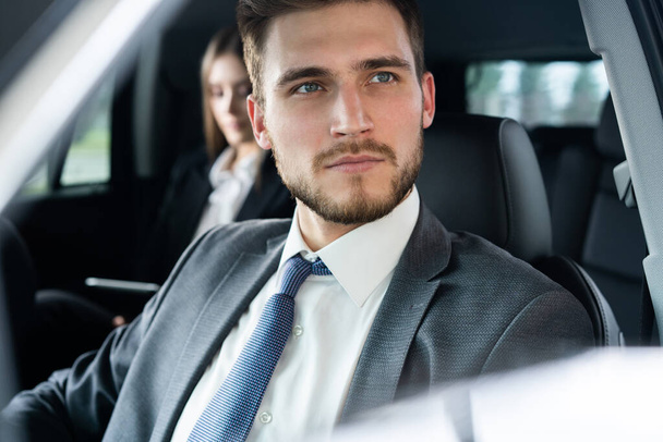 Success in motion. Handsome young man in full suit smiling while driving a car. - Valokuva, kuva