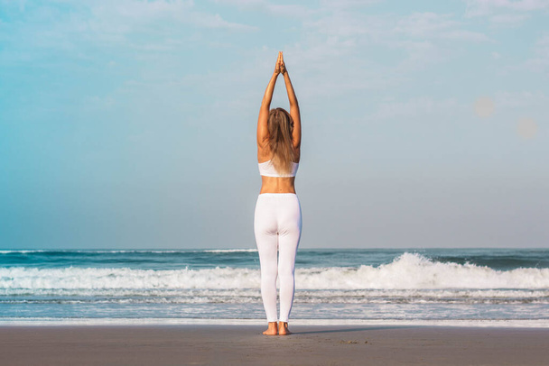 Девушка в белой одежде стоит на берегу моря и занимается йогой и медитацией
 - Фото, изображение