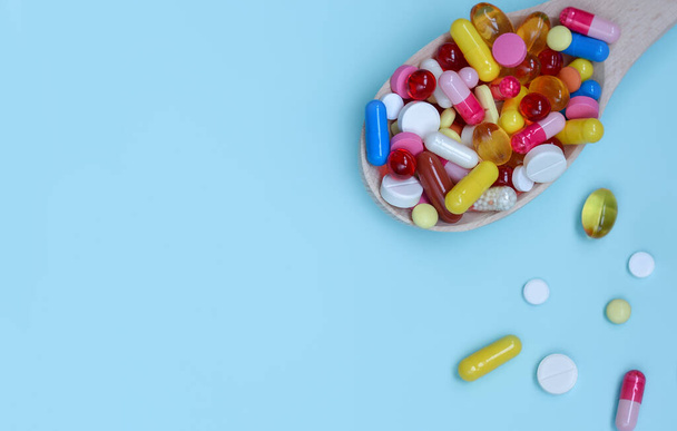 Barevné rozmanité farmaceutické kapsle, tablety a pilulky v dřevěné lžíci izolované na modrém pozadí. Doplněk stravy zdravotní produkt.Kopírovat prostor pro text. - Fotografie, Obrázek