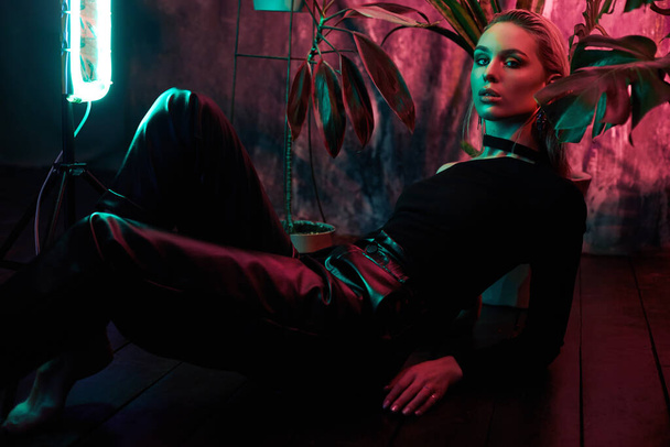 Fashion woman sitting on the floor in tropical foliage neon light. Wet hair, perfect figure and makeup. Pink and green neon color. Beautiful girl and monstera leaves - Fotografie, Obrázek