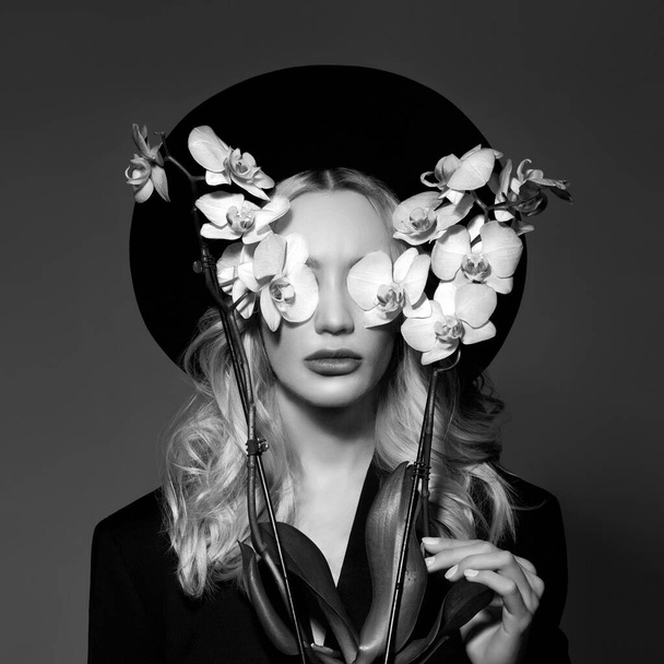 Portrait of a Blonde woman in a large round black hat, an Orchid flower in her hands - Fotografie, Obrázek