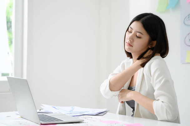 Концепція офісного синдрому. Молода азіатська бізнес-леді відчуває біль в шиї після тривалої роботи на комп'ютерному ноутбуці
 - Фото, зображення