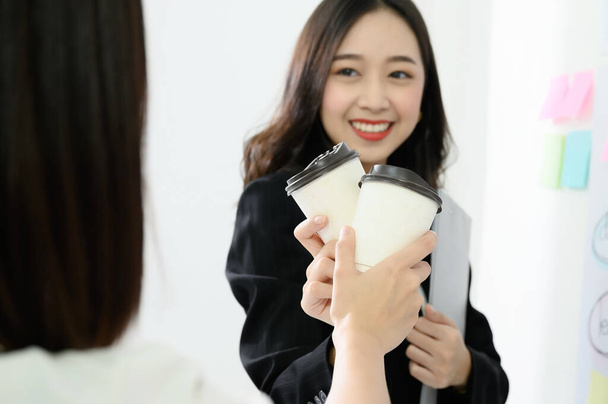 Duas mulheres asiáticas bonitas do negócio celebram seu sucesso do trabalho fazendo um clink de uma xícara de café, copo de papel. - Foto, Imagem