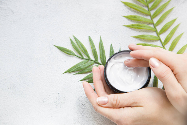 Flatlay. Woman putting nutritious cream on her hands on white background among jar of cosmetic cream, leaf palm branch. woman uses moisturizer for the skin. Copy space - Photo, image