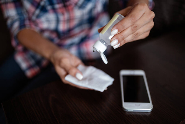 Cleaning a mobile cell phone with a disposable antibacterial wipe during coronavirus pandemic emergency using hand sanitizer. Health safety protection, home disinfection and quarantine concept - Photo, Image