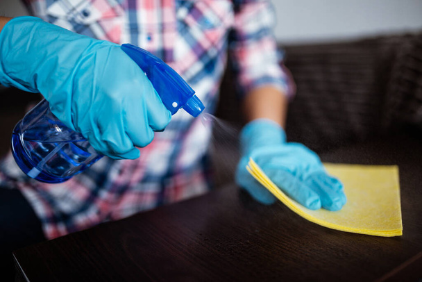 Очистка тёмной поверхности стола с помощью моющего средства, синих резиновых перчаток и жёлтой посуды на рабочей поверхности. Антибактериальная работа против коронавируса. Концепция гигиены, дезинфекции и здравоохранения
 - Фото, изображение