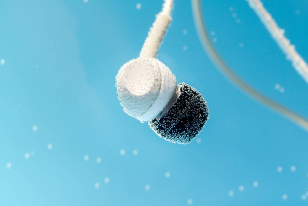Headphones under water on blue background. Listening to music, waterproof accessory - Photo, image