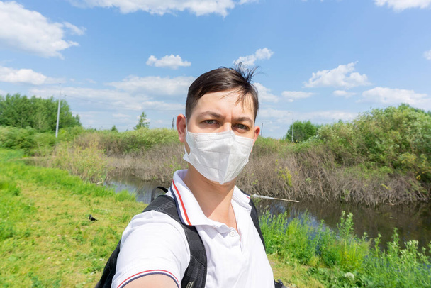 Портрет молодого человека в медицинской маске стоит у природы. close up, corona virus - Фото, изображение