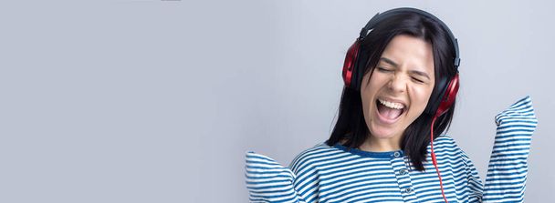 Una joven con un chaleco a rayas está escuchando música con auriculares rojos en un estudio y bailando
. - Foto, imagen