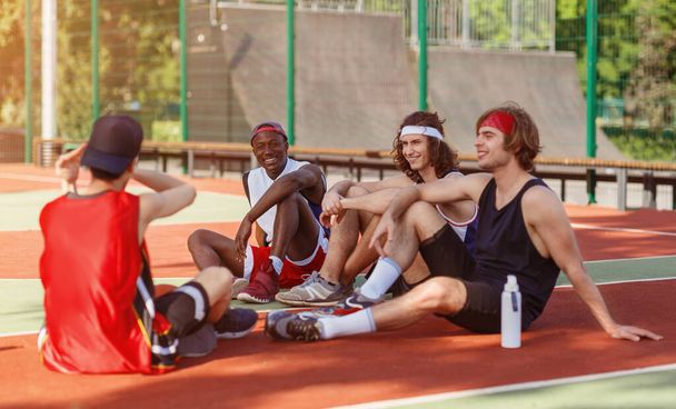 Multiethnic basketball team resting on outdoor arena after their game - Foto, immagini