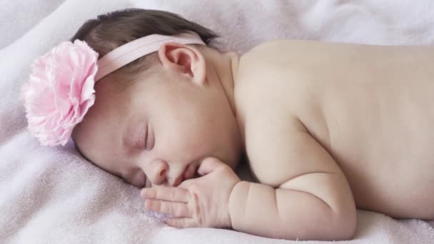 infanzia, infanzia, sviluppo, medicina e concetto di salute volto primo piano di una neonata nuda addormentata sdraiata sul suo stomaco con una benda e un fiore sulla testa su uno sfondo rosa. - Filmati, video