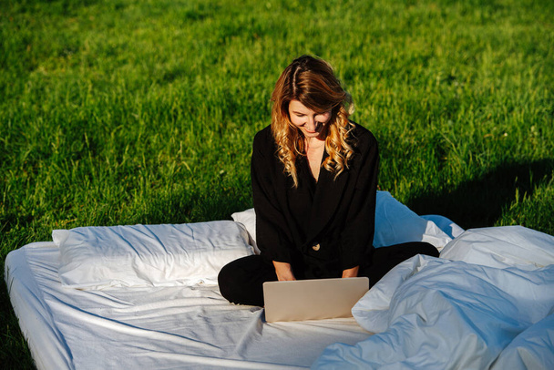 Satisfied, pleased woman working on laptop, sitting cross-legged in bed outdoors - Photo, image