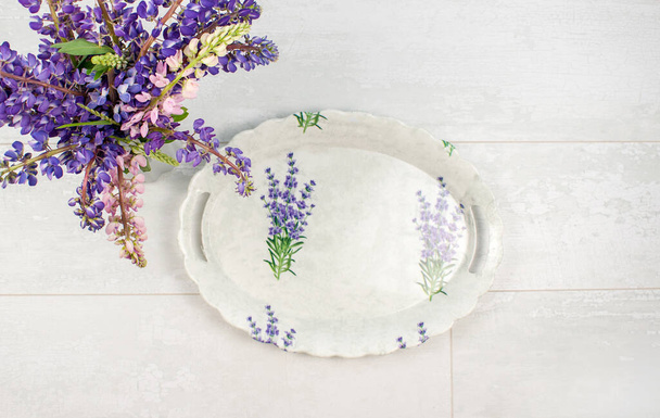 Empty oval tray for serving the table in vintage style. Flat lay home decoration. Vase with bouquet of flowers on a light wooden background or table. - Photo, image