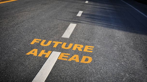 Future ahead word with white dividing lines on black asphalt road surface with sunlight, business challenge concept and effort idea - Photo, Image