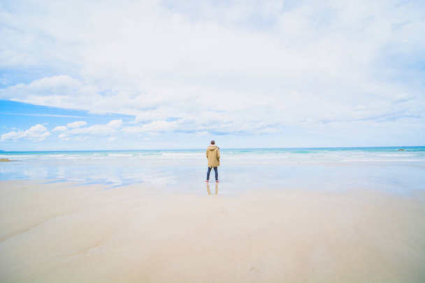 young man with arms open contemplating the ocean in mainly cloudy day - Fotoğraf, Görsel