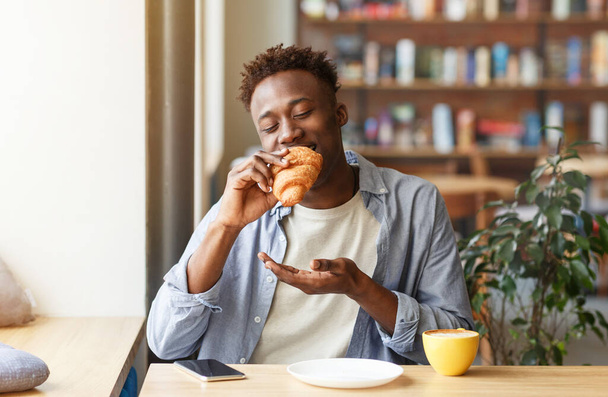 Funky musta kaveri syö croissant kahvia viihtyisässä kahvilassa - Valokuva, kuva