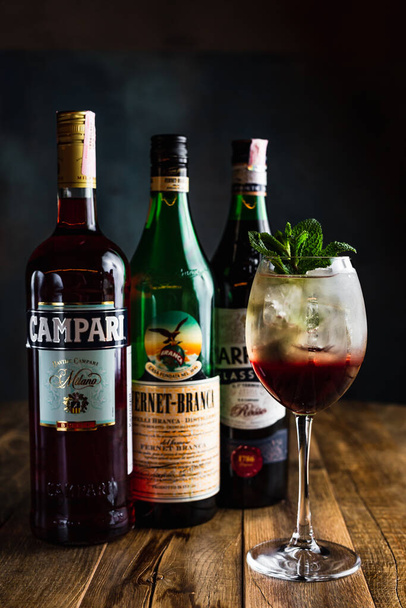 Belarus, Minsk - 12.03.2020: a refreshing layered iced cocktail in a wine glass garnished with mint, a bottle of Campari, Fernet-Branca and Carpano Classico vermouth - Zdjęcie, obraz