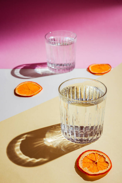 A very bright vertical photo of two rocks glasses of water, direct hard light with harsh shadows, orange chips - Fotografie, Obrázek