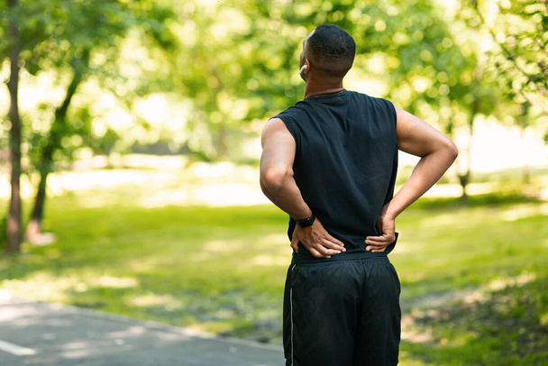 Millennial τύπος στα αθλητικά που πάσχουν από πόνο στην πλάτη wgilejogging στο πάρκο, κενό χώρο - Φωτογραφία, εικόνα