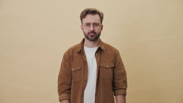 A serious young unshaven man is showing banknotes and credit card isolated over beige wall background in studio - Filmagem, Vídeo