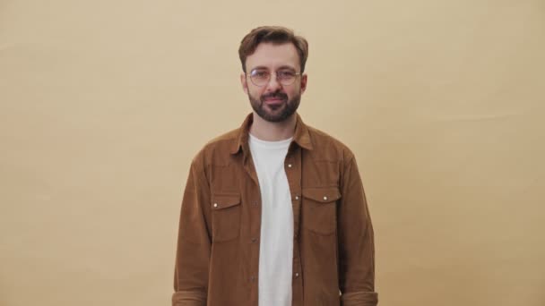 A happy pleased young unshaven man is showing his colorful purchases and credit card isolated over beige wall background in studio - Imágenes, Vídeo