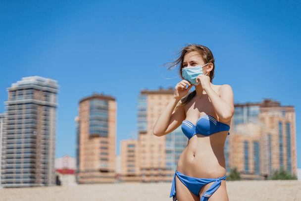 Blondes Mädchen in Bademode trägt Maske am Strand in der Sommersonne - Foto, Bild