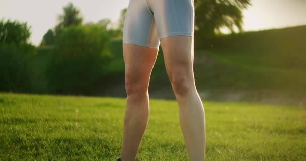 Uma mulher desportiva num parque agachada com halteres nas mãos ao pôr-do-sol. Treino de peso ao ar livre. Fitness em um parque público no verão de coxas e pernas
. - Filmagem, Vídeo