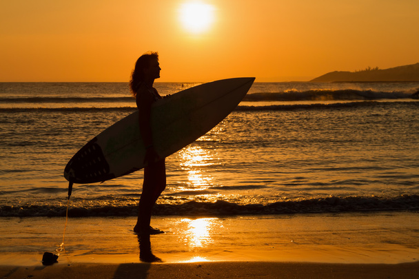 Rear view of beautiful sexy young woman surfer girl in bikini with white surfboard on a beach at sunset or sunrise - Fotó, kép
