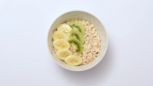 Stop motion animation of bowl with cereal, milk, fruits and nuts on white  - Πλάνα, βίντεο