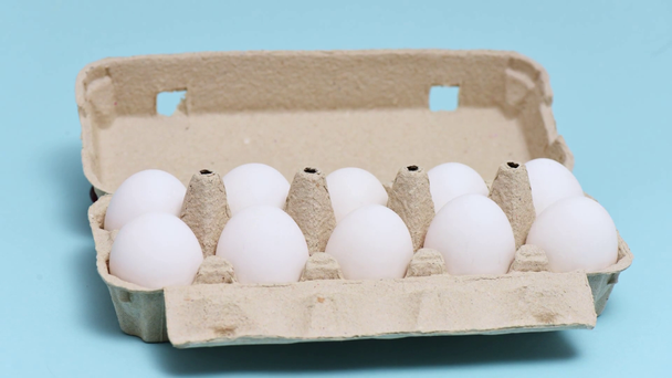 Διακοπή κίνησης κινουμένων σχεδίων των αυγών κοτόπουλου σε κουτί αυγών σε μπλε - Πλάνα, βίντεο