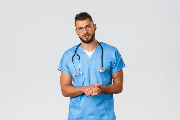 Healthcare workers, medicine, covid-19 and pandemic self-quarantine concept. Professional doctor, surgeon or physician in clinic talking to patient with serious worried face, wear blue scrubs - Photo, Image