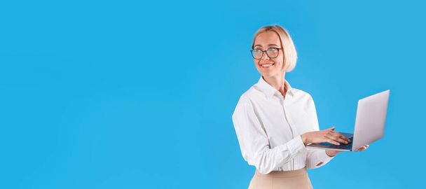 Happy millennial business lady with modern laptop on blue background, space for text - Photo, Image
