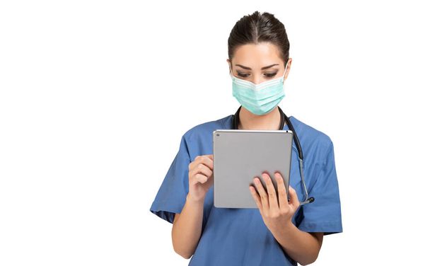 Masked young nurse doctor using a tablet, isolated on white background  - Foto, afbeelding