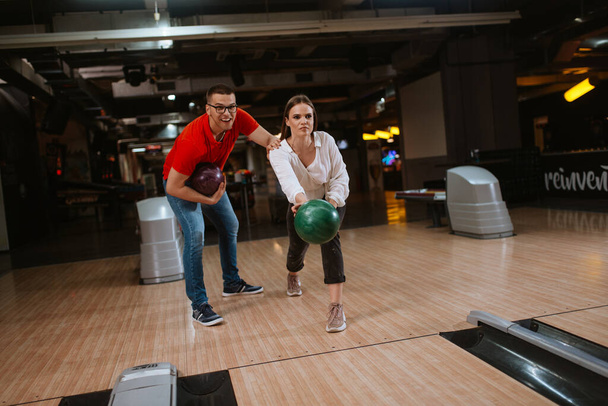 Um belo casal caucasiano amoroso jogando bolas na pista de boliche. Namorado e namorada no clube de bowling
 - Foto, Imagem