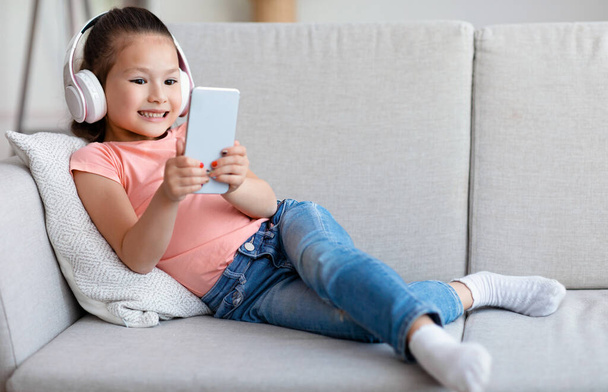 Menina usando telefone jogar jogo móvel deitado no sofá interior
 - Foto, Imagem