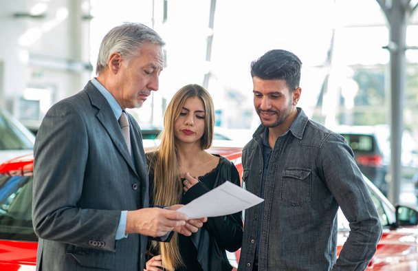 Happy young family talking to the salesman and choosing their new car in a showroom - 写真・画像