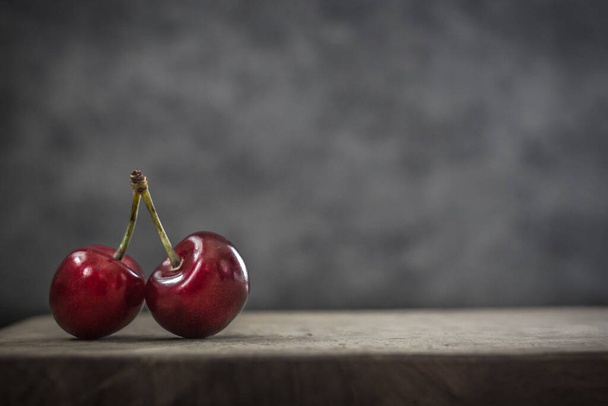 Red berries. Ripe sweet cherries. Food that is good for the brain improves memory and skin. Retinol-rich foods. Two cherries on one branch. Object shooting. Still life in fashion style. Red on gray. - Photo, Image