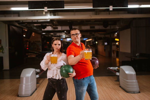 Uma mulher caucasiana e um homem na pista de bowling com canecas de cerveja. Amor e boliche
 - Foto, Imagem