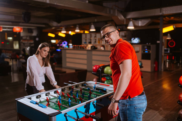 A beautiful caucasian girl and a man with glasses play table football in the playroom. Love and fun time - Photo, Image