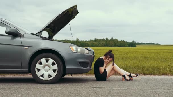 Una chica molesta en un vestido corto se sienta en el pavimento y trata de llamar al servicio de emergencia por teléfono después de que su coche se rompió en la carretera. Movimiento lento
. - Metraje, vídeo