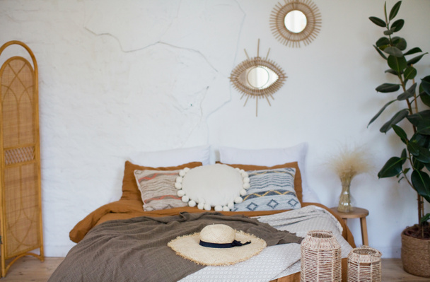 Chambre bohème avec des décorations en matériaux naturels. Lit avec différents oreillers et couvertures, miroirs sur un mur - Photo, image