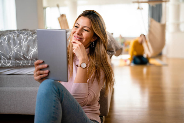Attractive young woman using digital tablet and smiling while sitting at home - Photo, Image
