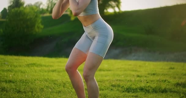 Une femme accroupie avec des haltères dans le parc au coucher du soleil se jette sur le côté. Motivation et entraînement sportif. Une femme célibataire fait des exercices au coucher du soleil en été - Séquence, vidéo