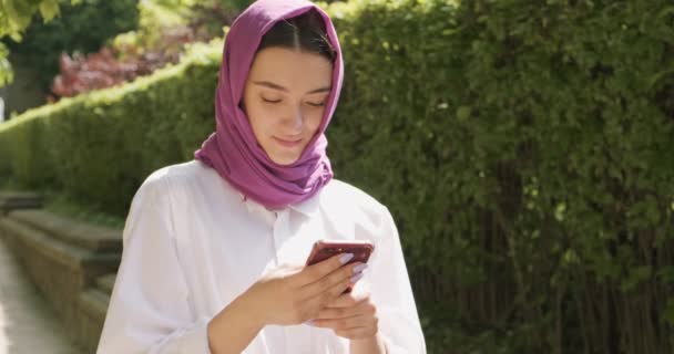 Gyönyörű fiatal nő néz okostelefon, visel hagyományos fejkendő. Vonzó nő a hidzsáb - Felvétel, videó