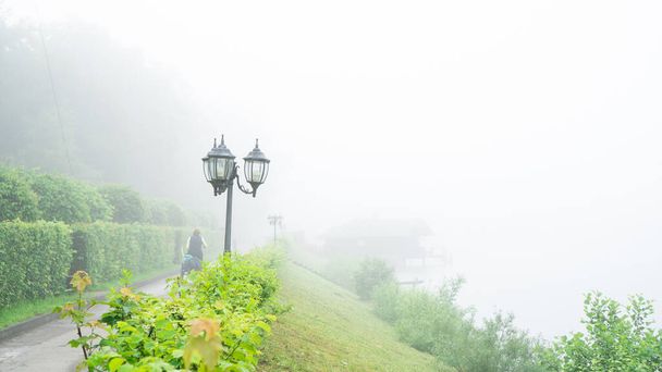caminho com lanternas e uma encosta verde para o lago com nevoeiro de evaporação pesado na manhã de verão. contexto
 - Foto, Imagem