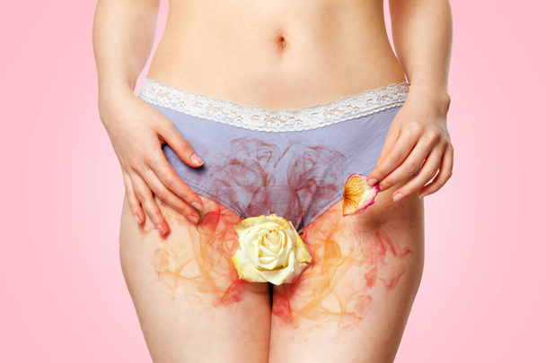A woman in her underwear holds a white rose flower between her legs, which exudes an unpleasant smell, and a withered petal in her hand. Close up. Pink background. Concept of menopause and women's health problems. - Photo, Image
