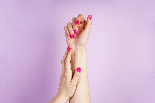 Prachtige manicure. Mooie handen van een jonge vrouw op een paarse achtergrond.  - Foto, afbeelding