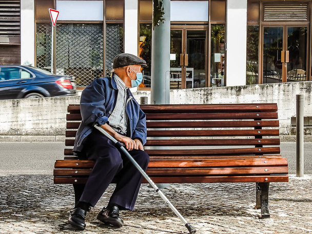 An old man sitting on a bench during a pandemic with a mask on - Foto, immagini